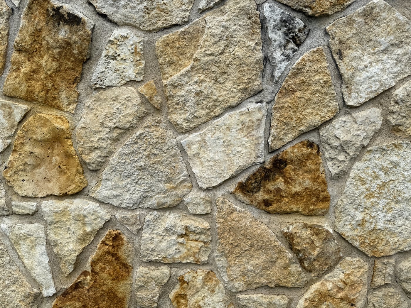 Closeup of a cream, gold, and rust random-shape mosaic stone wall — tight irregular fit with hand-cut chopped faces