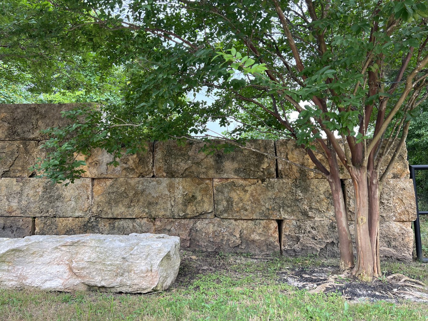 Stacked Cavestone boulder retaining wall with a crape myrtle and a single boulder accent stone in front