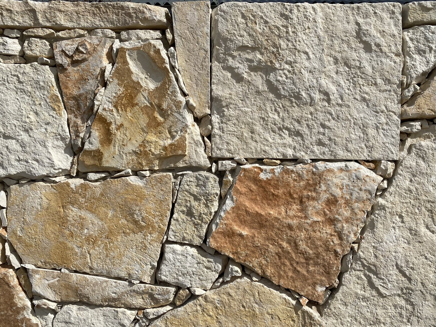 Closeup of a cream, gold, and rust random-shape mosaic stone wall with strong color variation in tight irregular joints