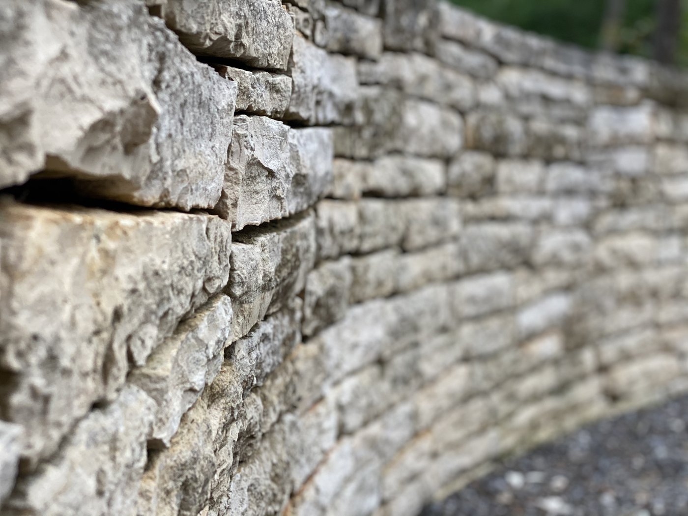 Dry-stacked cream-and-grey ledgestone retaining wall with a rough chopped face and tight horizontal courses — curving angle view