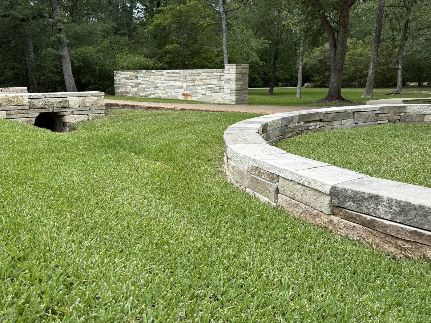 Curved Cream + Castle Grey 2-4-6 retaining wall with a flat cream cap, set into a grassy parklike landscape