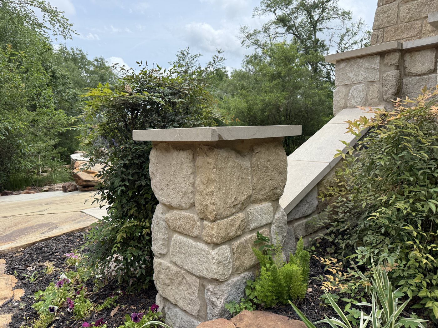 Rock-faced cream limestone column with a flat cream cap anchoring a stone garden wall surrounded by plantings