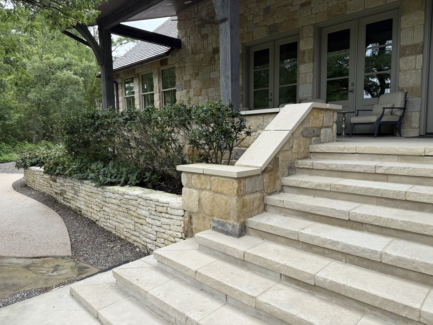 Cream stacked-ledge retaining wall with a flat-cap pillar leading into wide Granada Grey steps