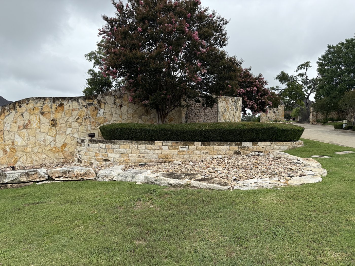 Entry monument with cream and gold random-shape mosaic wall and a coursed cream cap, framing a flowering crape myrtle