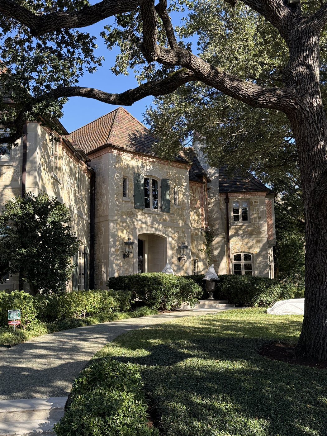 Old-World residence — Antique chopped random ashlar with terracotta tile roof, framed by mature oaks