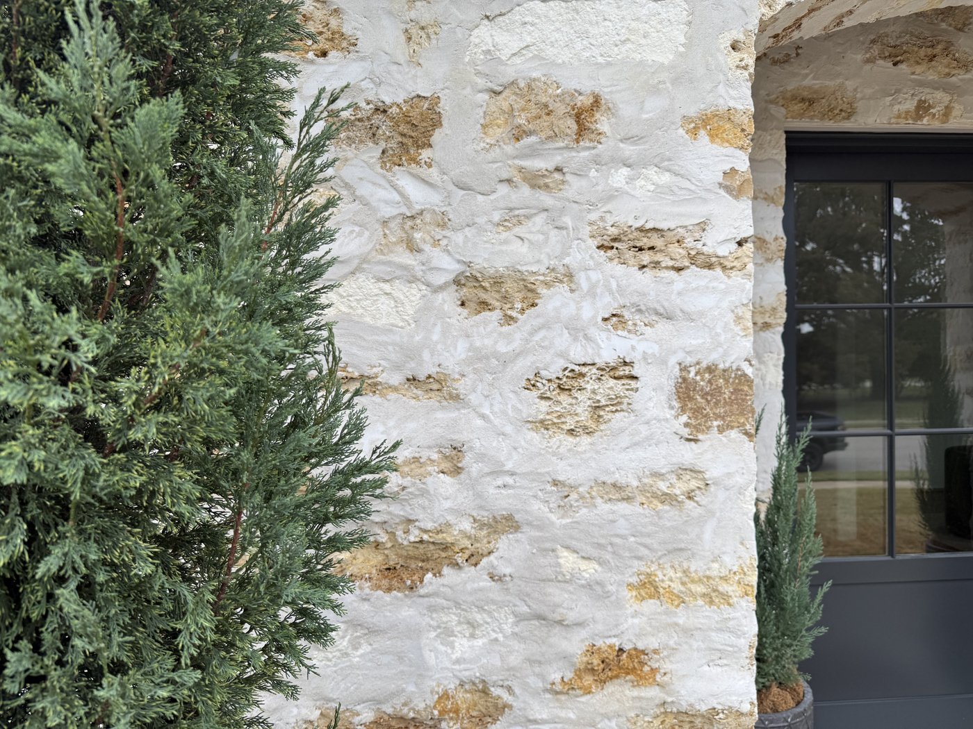 Italian villa — Cavestone heavy smear joint close-up softened by a cypress tree alongside an arched window