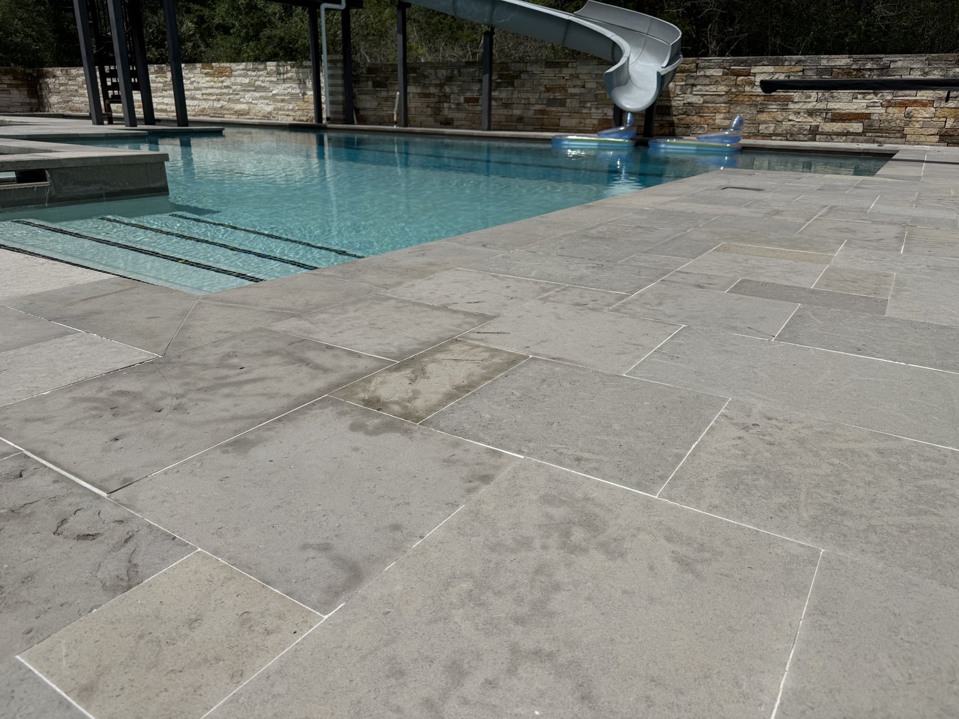 Pool deck in charcoal bush-hammered limestone — large dimensional pavers in a French pattern around a residential pool with water slide