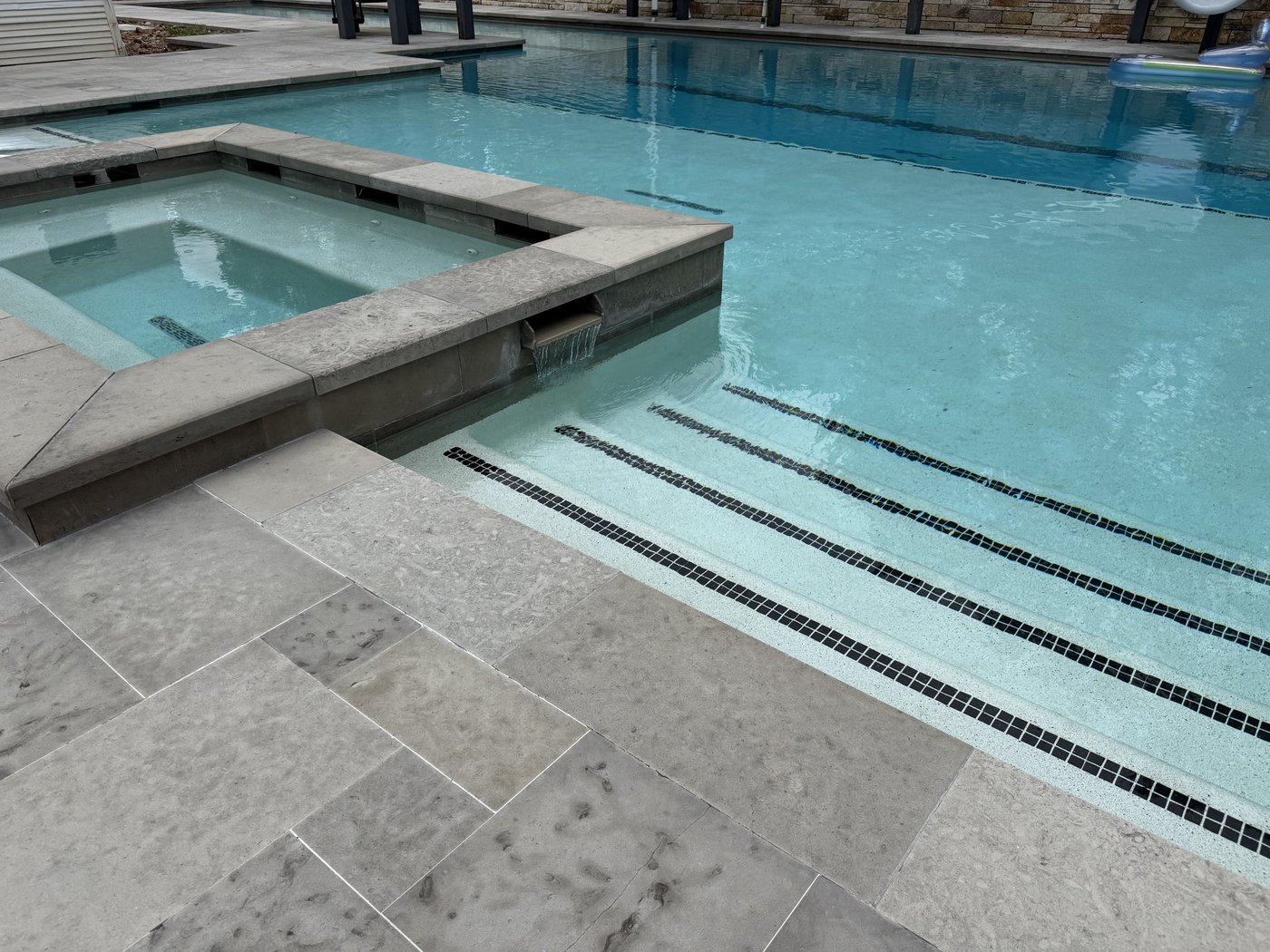 Charcoal bush-hammered pool deck — spa overflow and tanning ledge with custom-cut coping