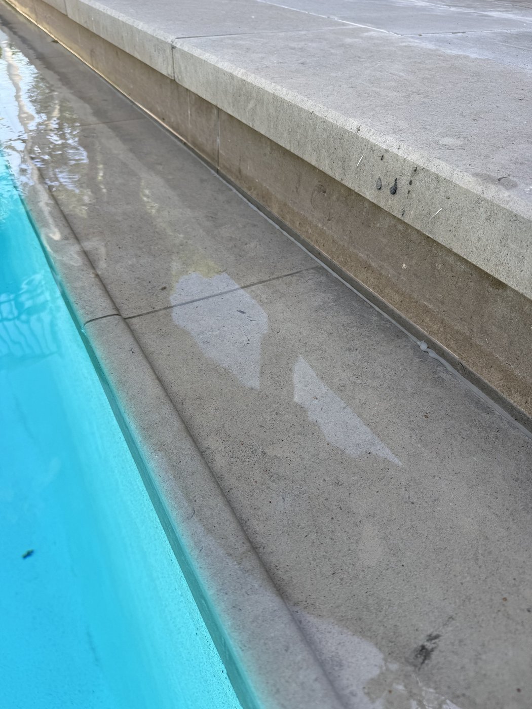 Custom carved grip edge in charcoal limestone under the pool waterline — chamfered profile for safer entry