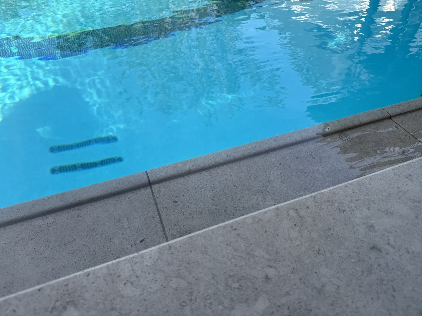 Charcoal limestone grip edge under water — angled view showing the carved profile transition from deck to pool