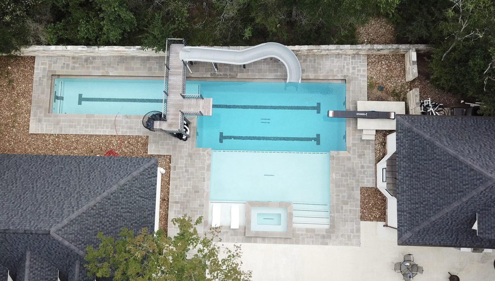 Aerial view of a residential pool with slide and tanning ledges — charcoal limestone pool decking, naturally aged grey from saltwater exposure