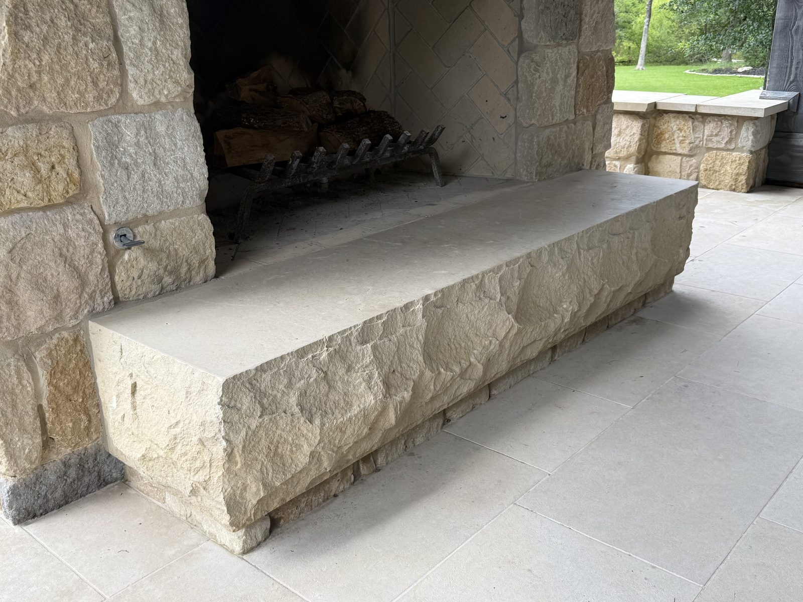 Outdoor fireplace — single massive hand-chiseled limestone hearth block, over 2,000 lbs, set on a French Chateau dimensional ashlar pedestal in front of a stone firebox