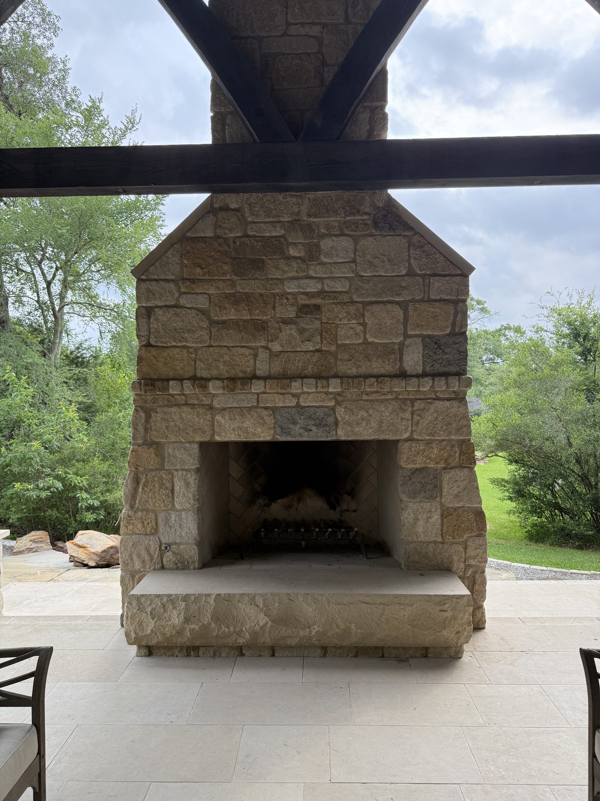 Outdoor fireplace — full elevation showing the chimney stack, rough-chiseled mantel slab, and the 2,000-pound hand-chiseled hearth block on its French Chateau pedestal
