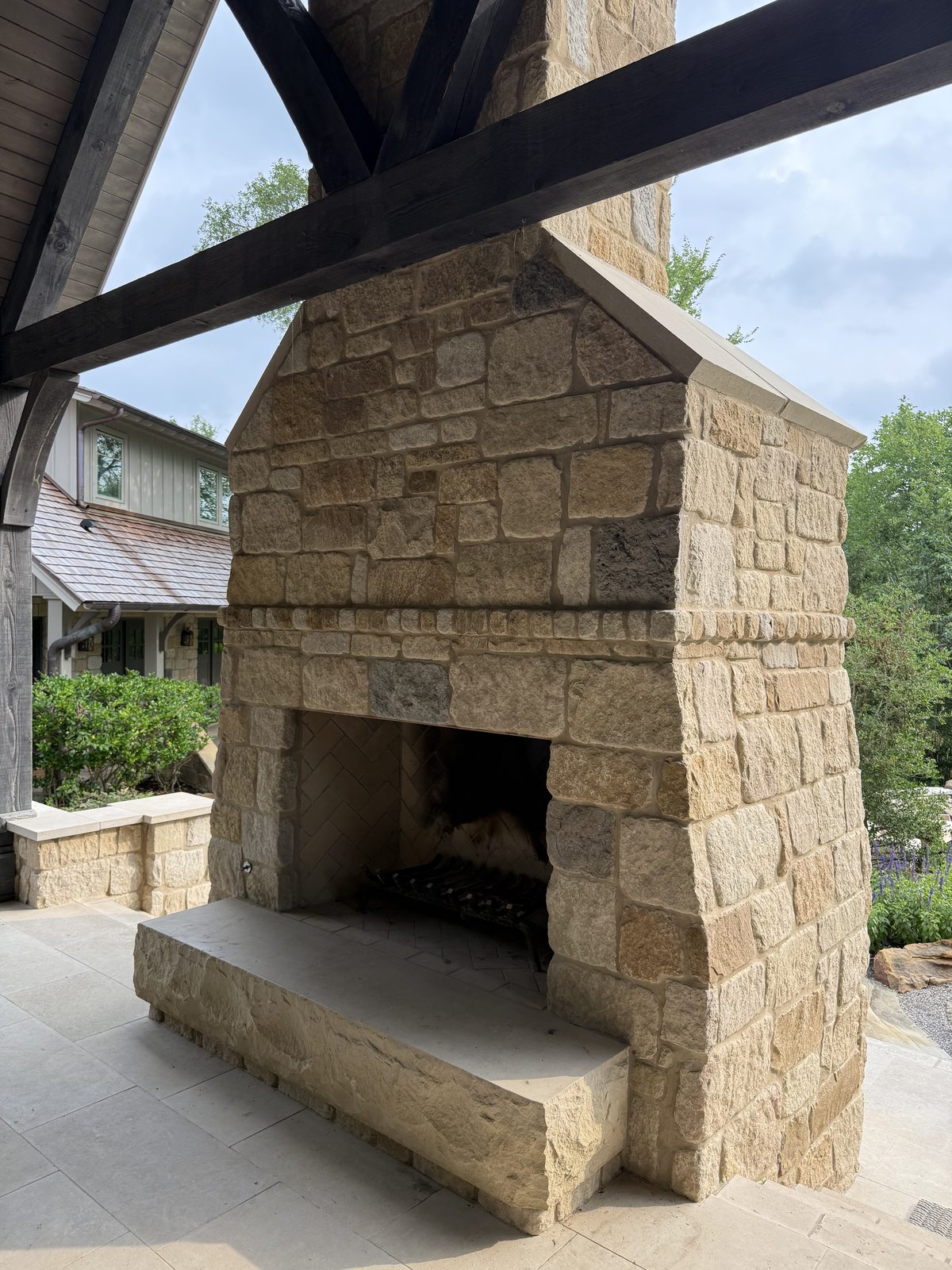 Outdoor fireplace — angled view from below showing the chimney cap, projecting mantel slab, and chiseled stone surround under a covered porch