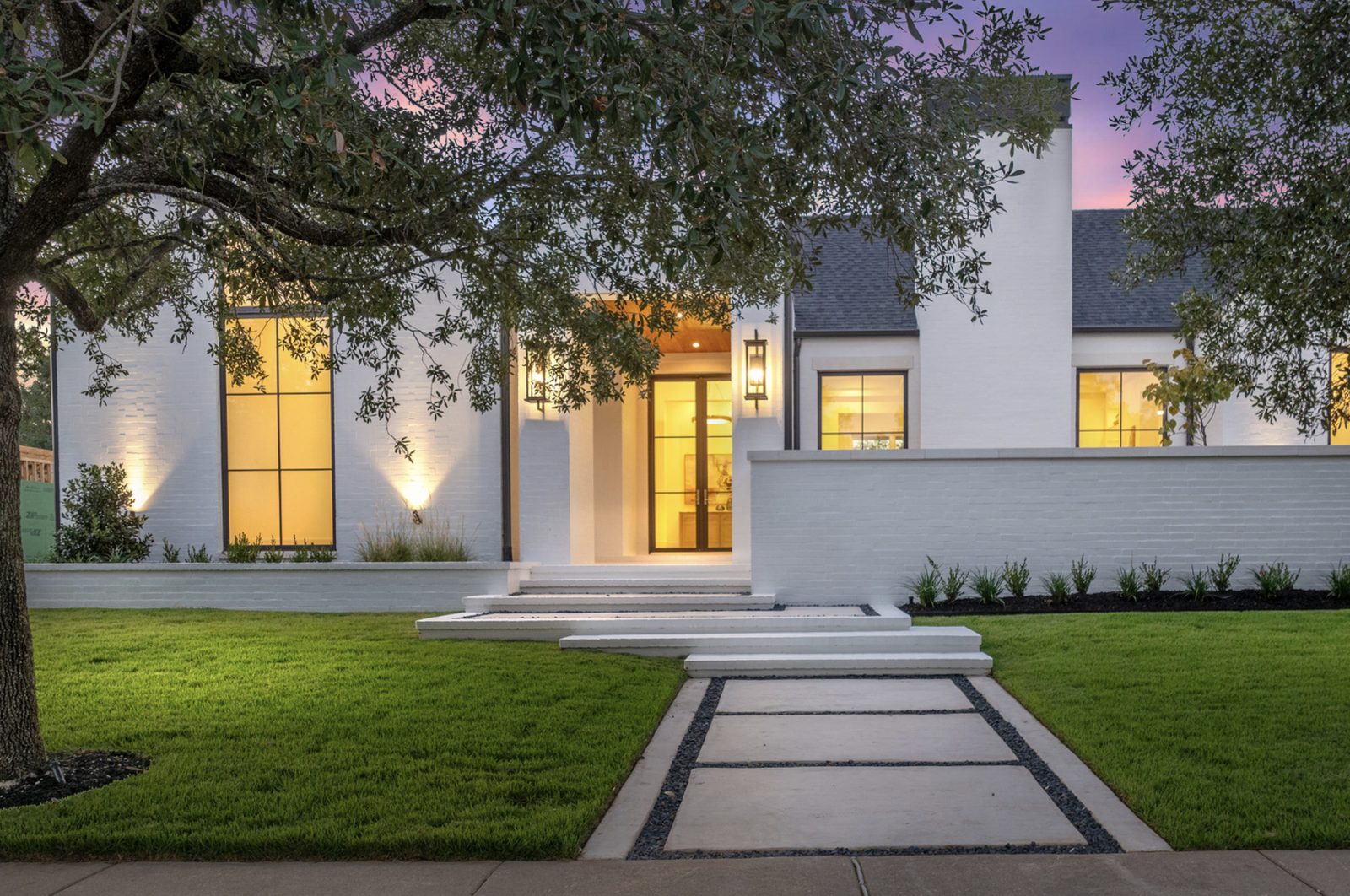 Modern white-brick residence at dusk — front entry with wide white limestone step slabs leading to the door and a concrete sidewalk approach