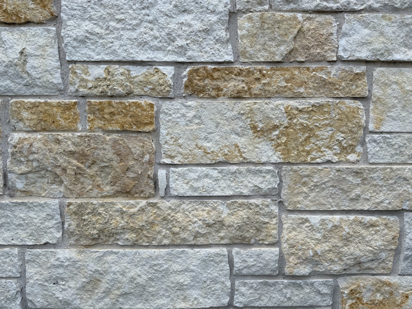 Goldstone close-up — cream limestone with golden-amber accent stones in a random ashlar pattern