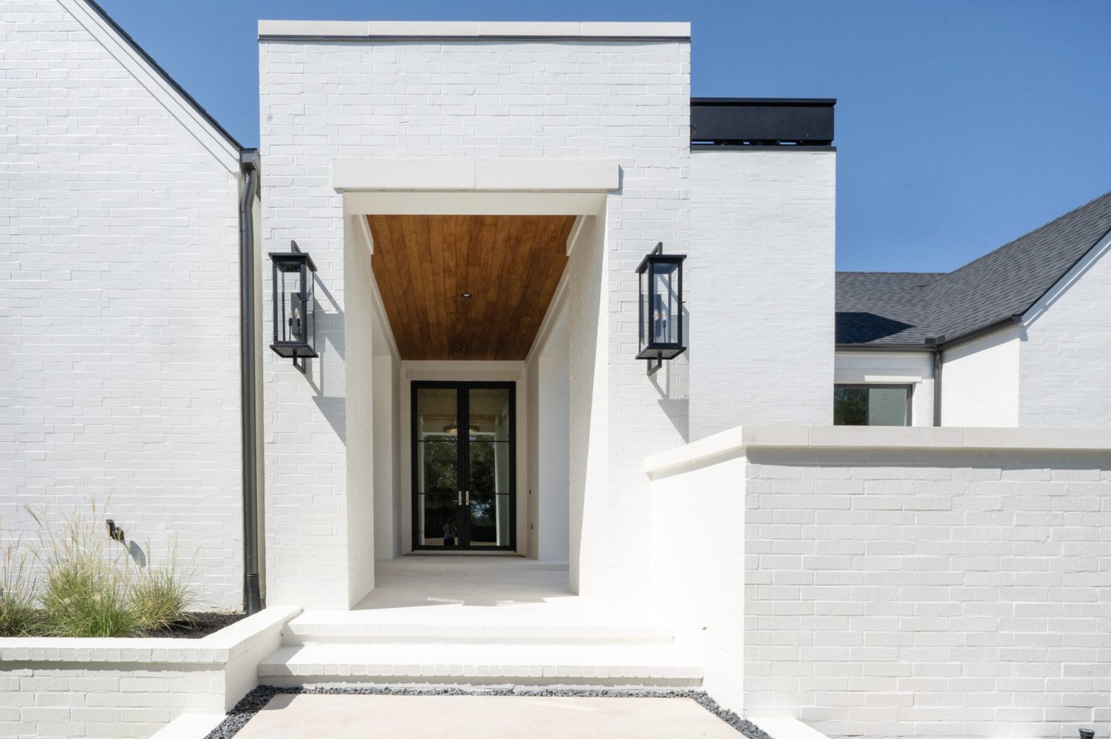 Modern white-brick residence entry — projecting white limestone header over the front door, white stone caps on flanking wing walls