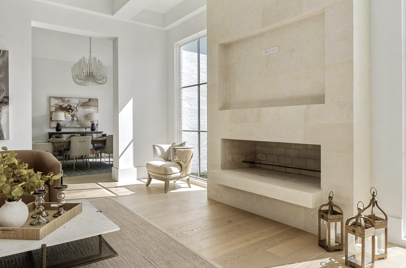 Modern living room — full-height Whitewing limestone fireplace surround with raised firebox, recessed niche above, lanterns on the hearth, and dining room beyond