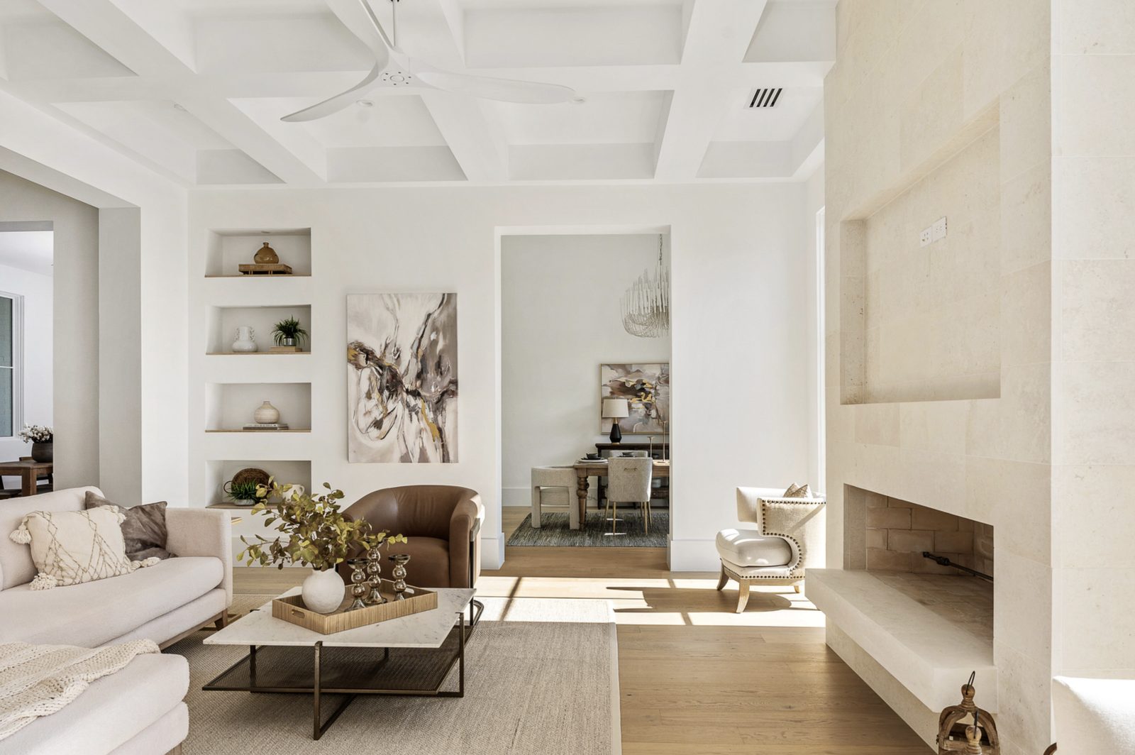 Living room with coffered ceiling — Whitewing limestone fireplace at right with raised firebox and niche, leather chair and bookshelves beyond