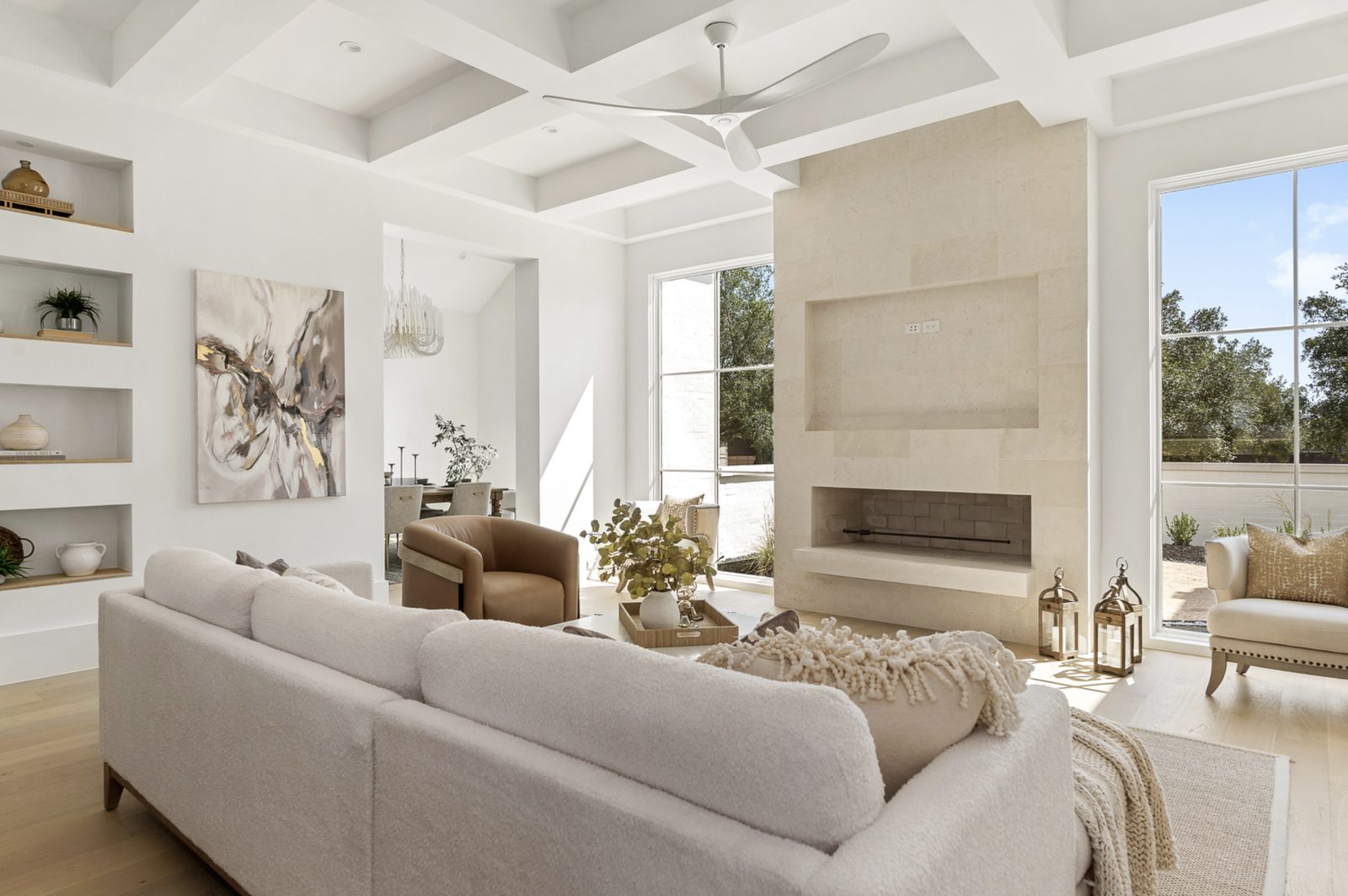 Living room — Whitewing limestone fireplace at center with raised firebox and recessed niche above, sofa and chair facing it, tall windows on either side