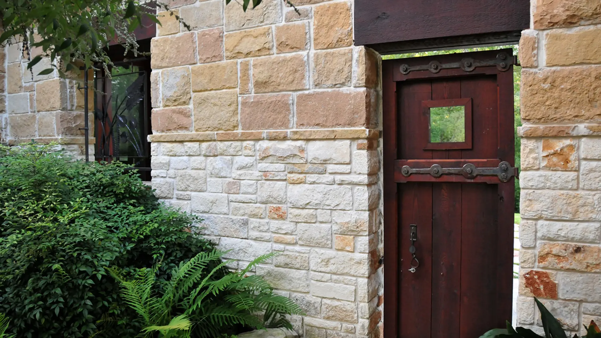 A brick wall with a door and plants in front of it.