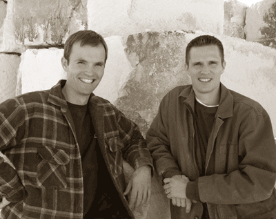 Two men posing for a picture in front of a wall.